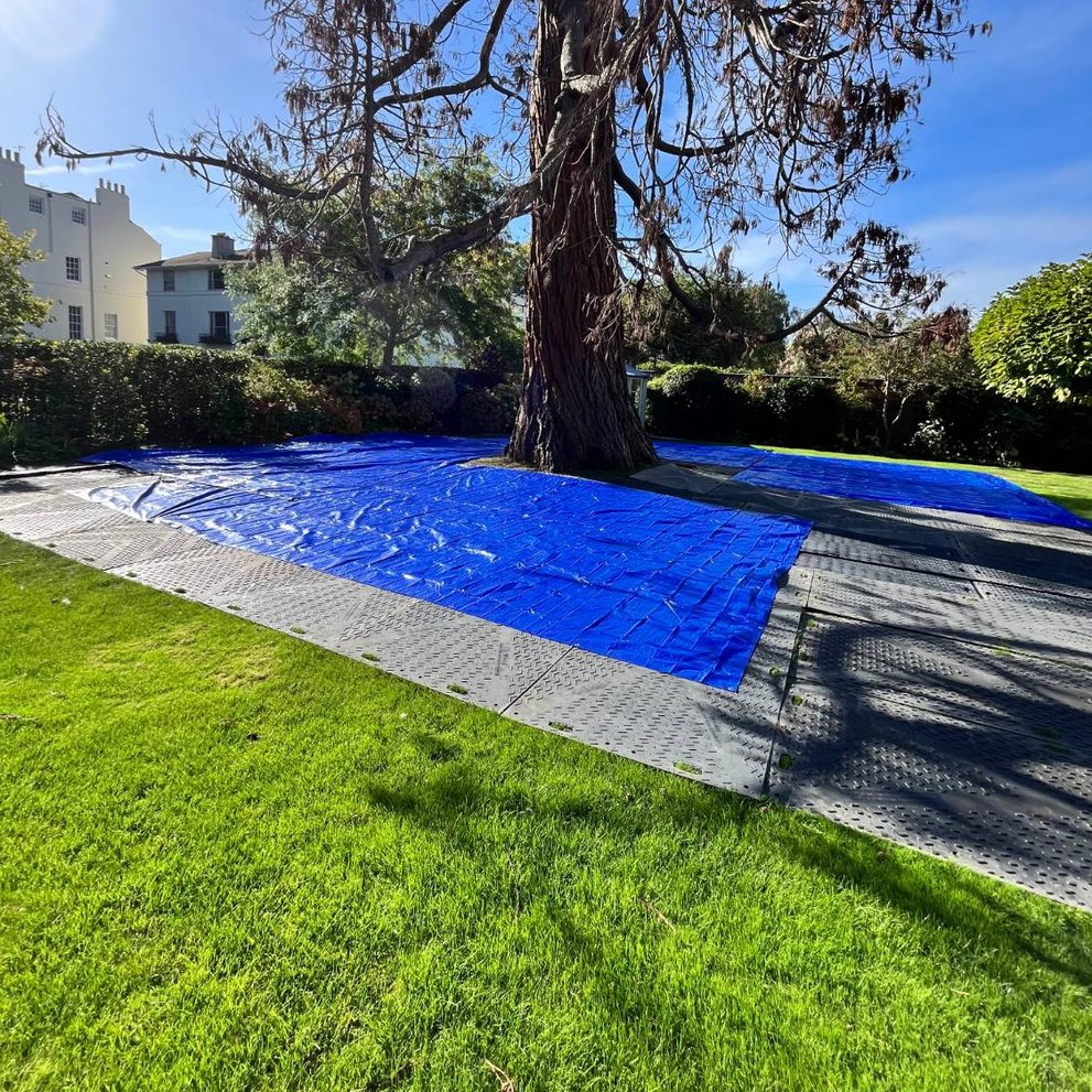 Ground protection mats and sheeting laid around a tree to protect the lawn